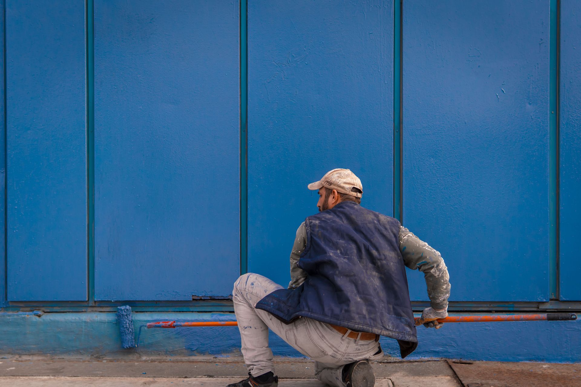 A construction worker paints a large blue wall outside, adding color and life.